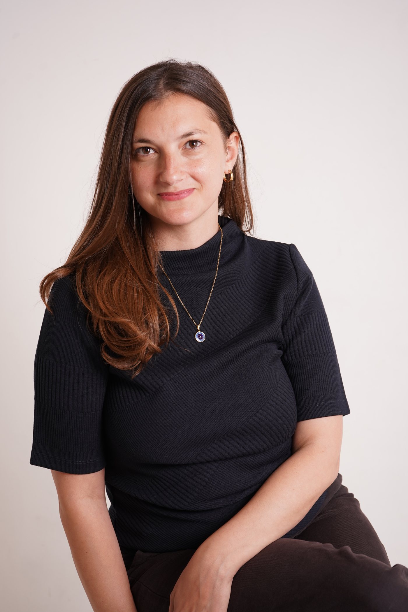 Author Chloe Cheimets, seated, wearing a dark ribbed top against a pale background.